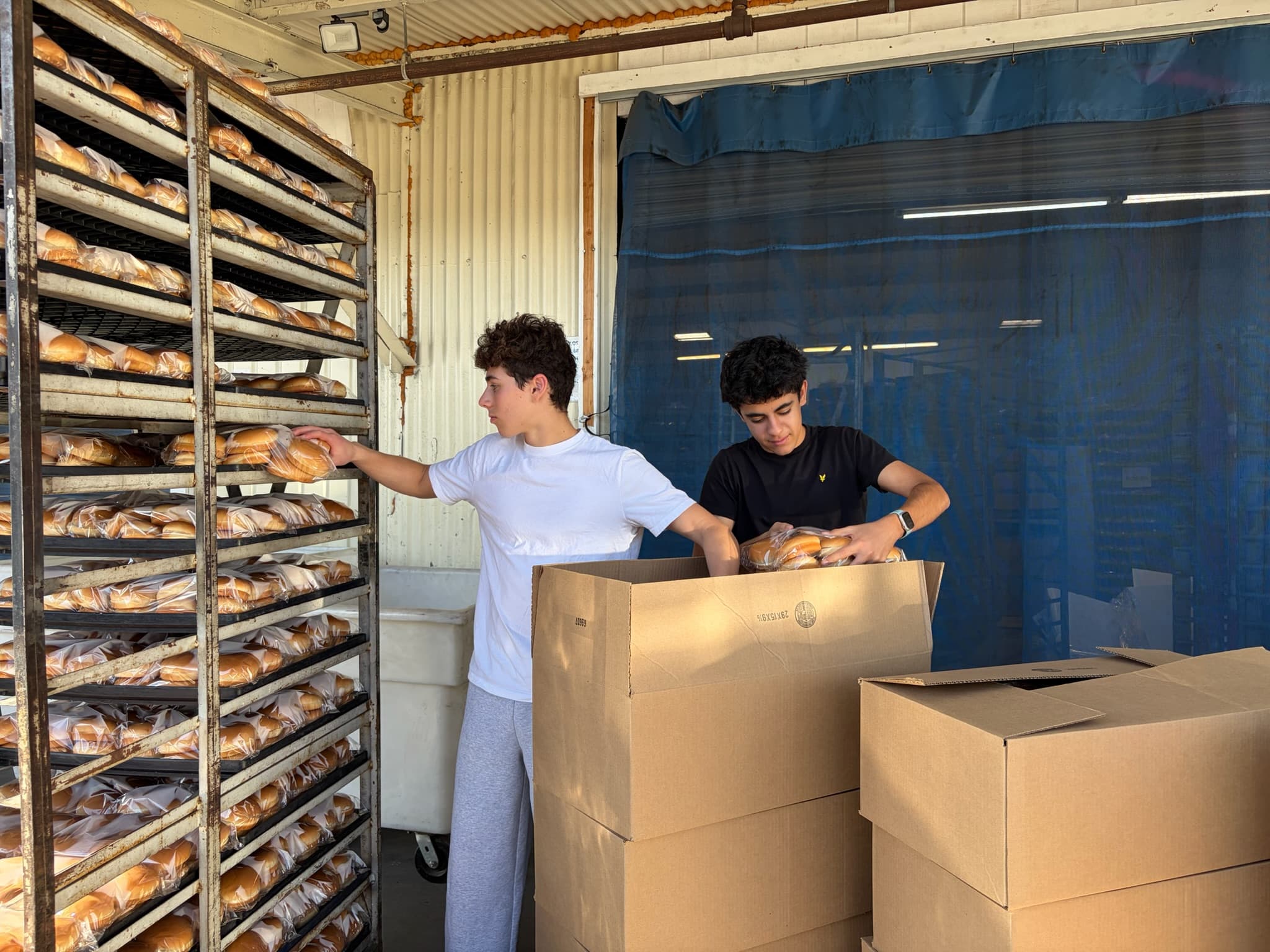 KneadLA volunteers packing fresh bread from a bakery rack into boxes